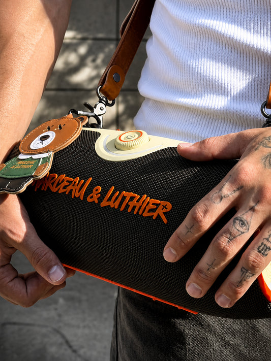 Close-up of the Rive Droite speaker held by a model, highlighting the orange logo and textured dark green fabric.
